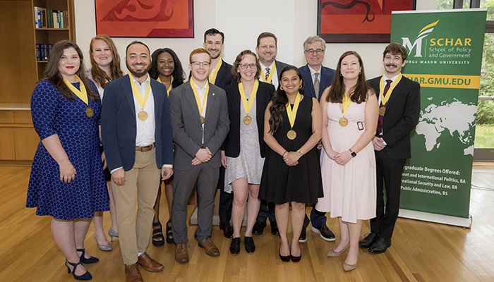 A group of well-dressed young people wearing yellow ribbons with gold medals smile for the camera.