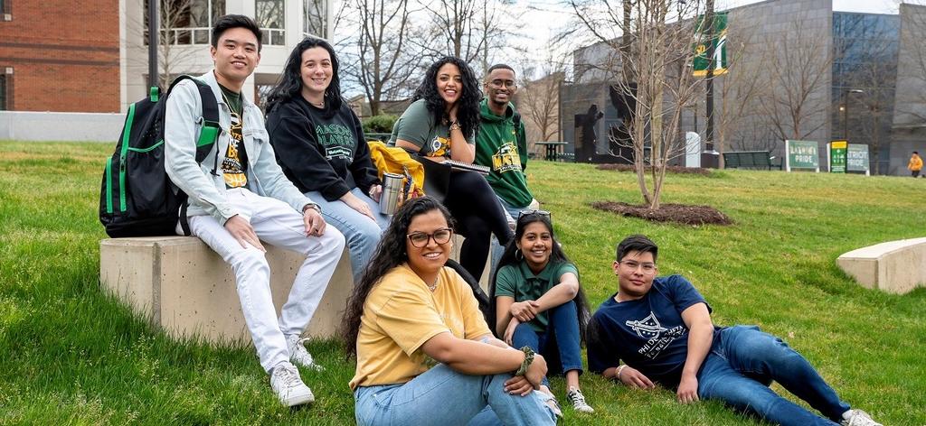 undergraduate students sitting on lawn and smiling at the camera