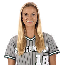 A woman with long blonde hair in a green and gray sports top with the number 18 on it smiles for the camera.