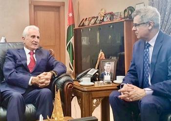 Two men in suits and ties sit on leather chairs in an office.