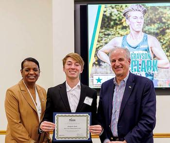 A young man in a suit jacket holds a certificate while being flanked by a woman and a man who are smiling.