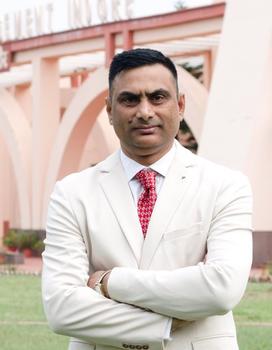 A man in a white jacket and red tie looks at the camera with his arms folded.