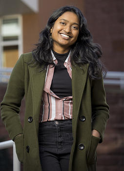 Schar School student Ruthu Josyula standing and smiling in front of a brick building while wearing a green jacket