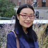 Ketian Zhang standing outside and smiling while wearing a blue blazer and glasses